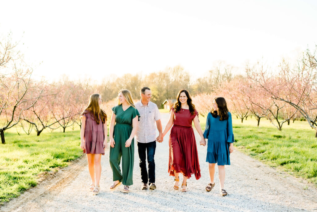 A family of five - a mom and dad with their three teenage daughters - walks in a blooming peach orchard in Jackson Missouri.