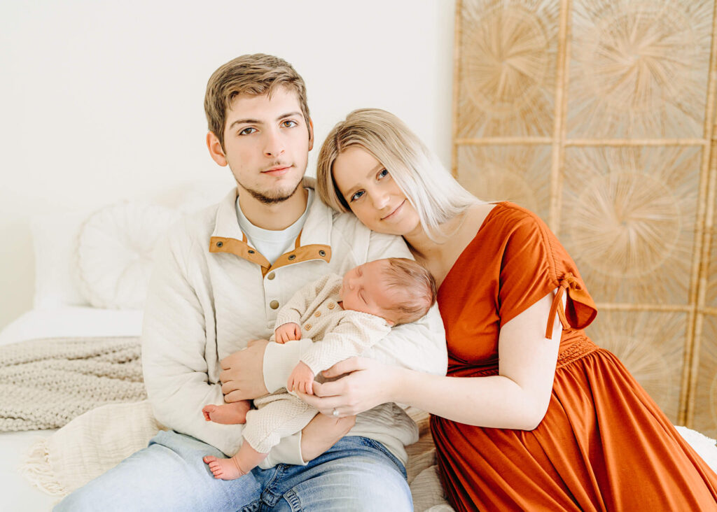 A new mom and dad pose with their newborn baby girl at a studio in Jackson Missouri. This photo is part of a blog post about choosing outfits for your family photos.