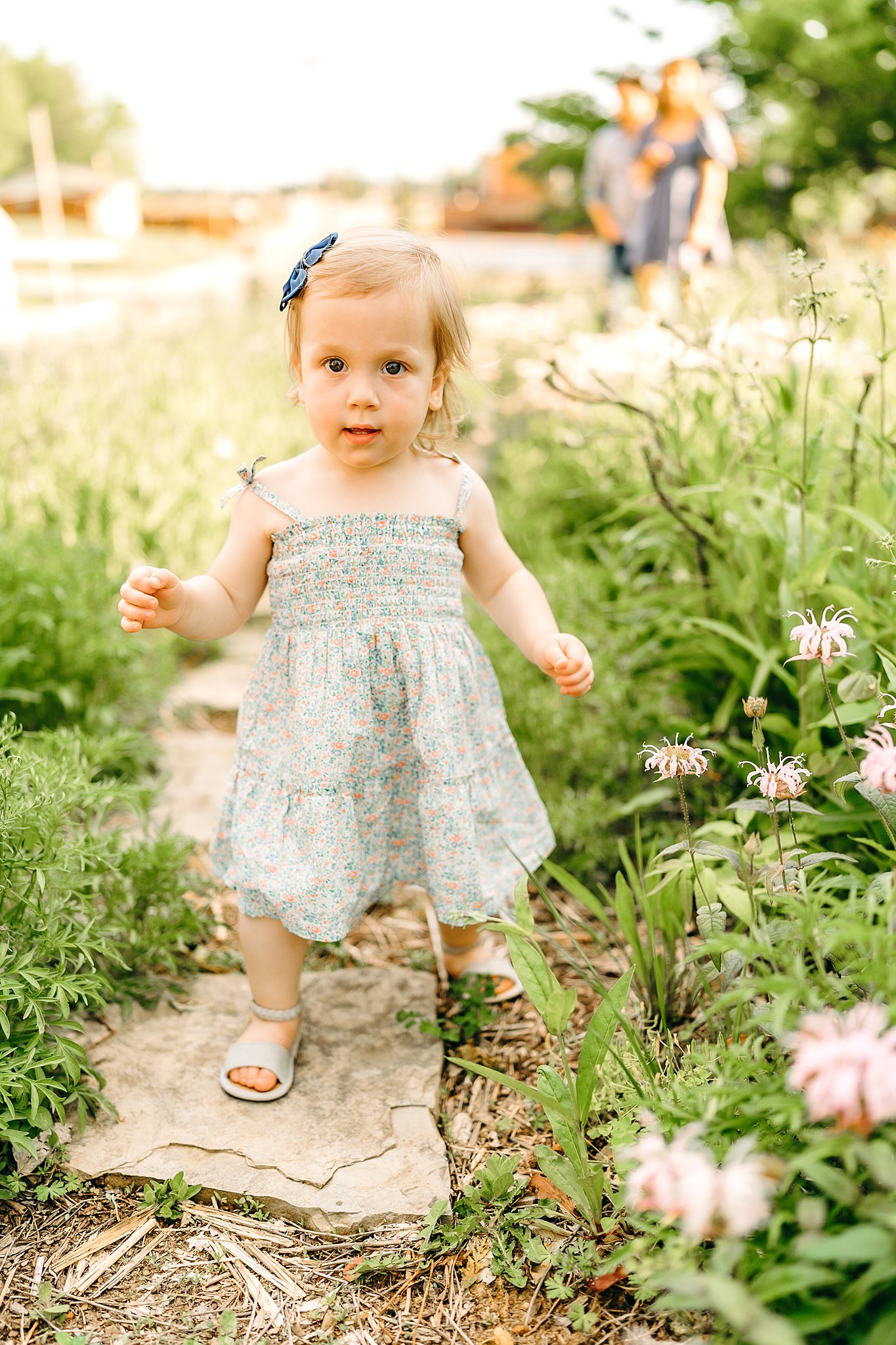A toddler girl stands on a stone path of a garden iin a blue dress and bow southeast missouri state parks