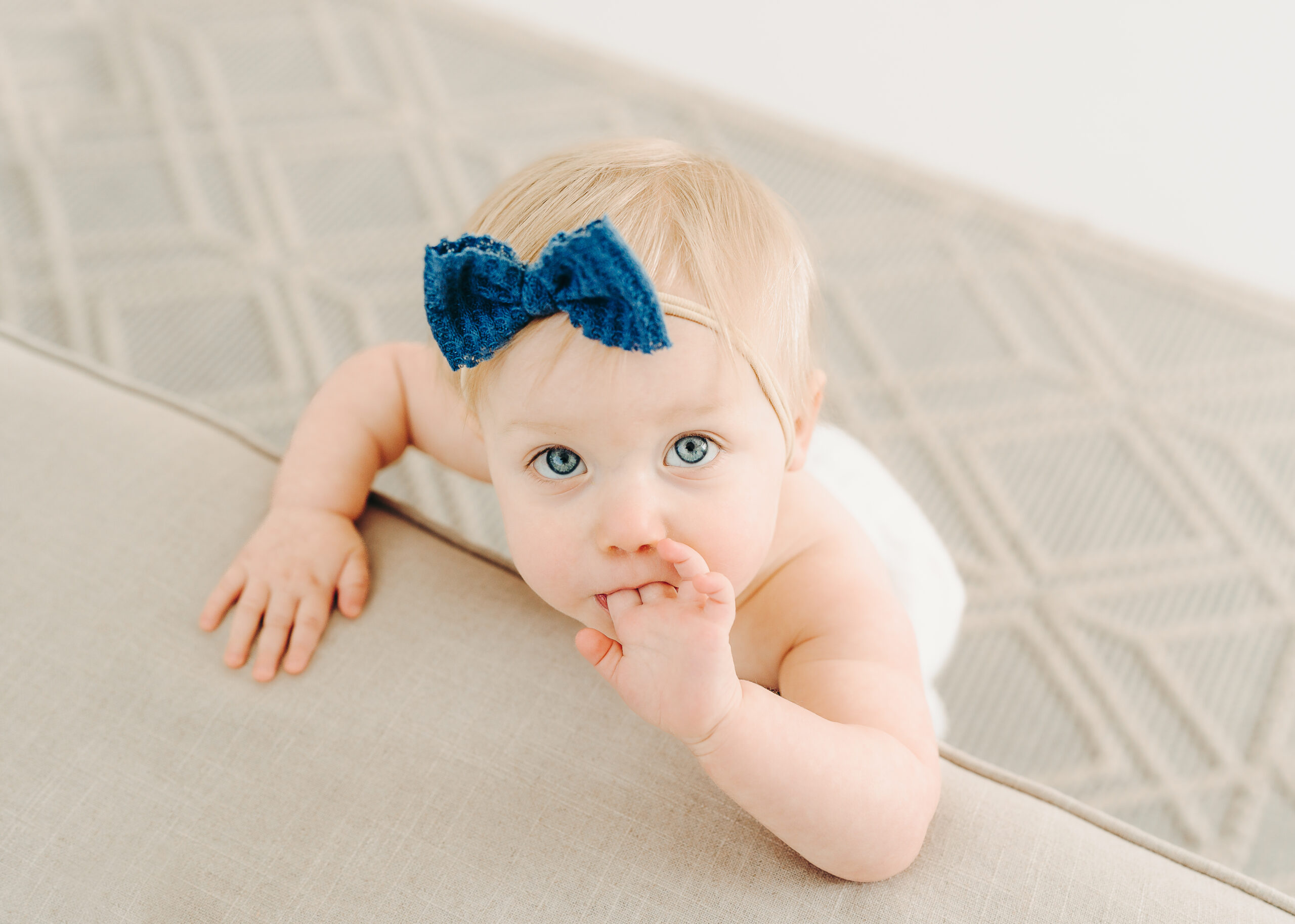 A baby girl looks up inquisitively at the camera wearing a blue bow.